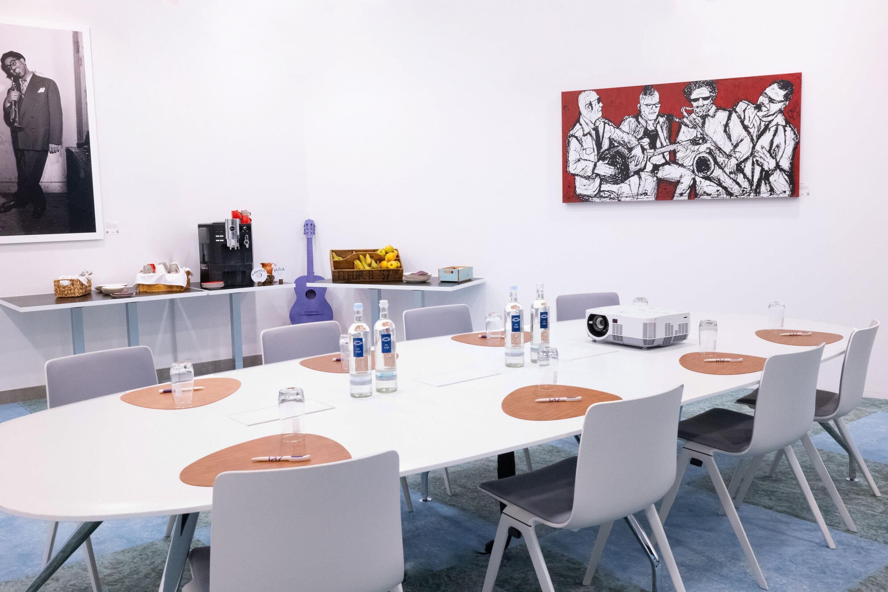 Une salle de conférence équipée d’une longue table, de chaises, d’un projecteur, de bouteilles d’eau et d’une machine à café.