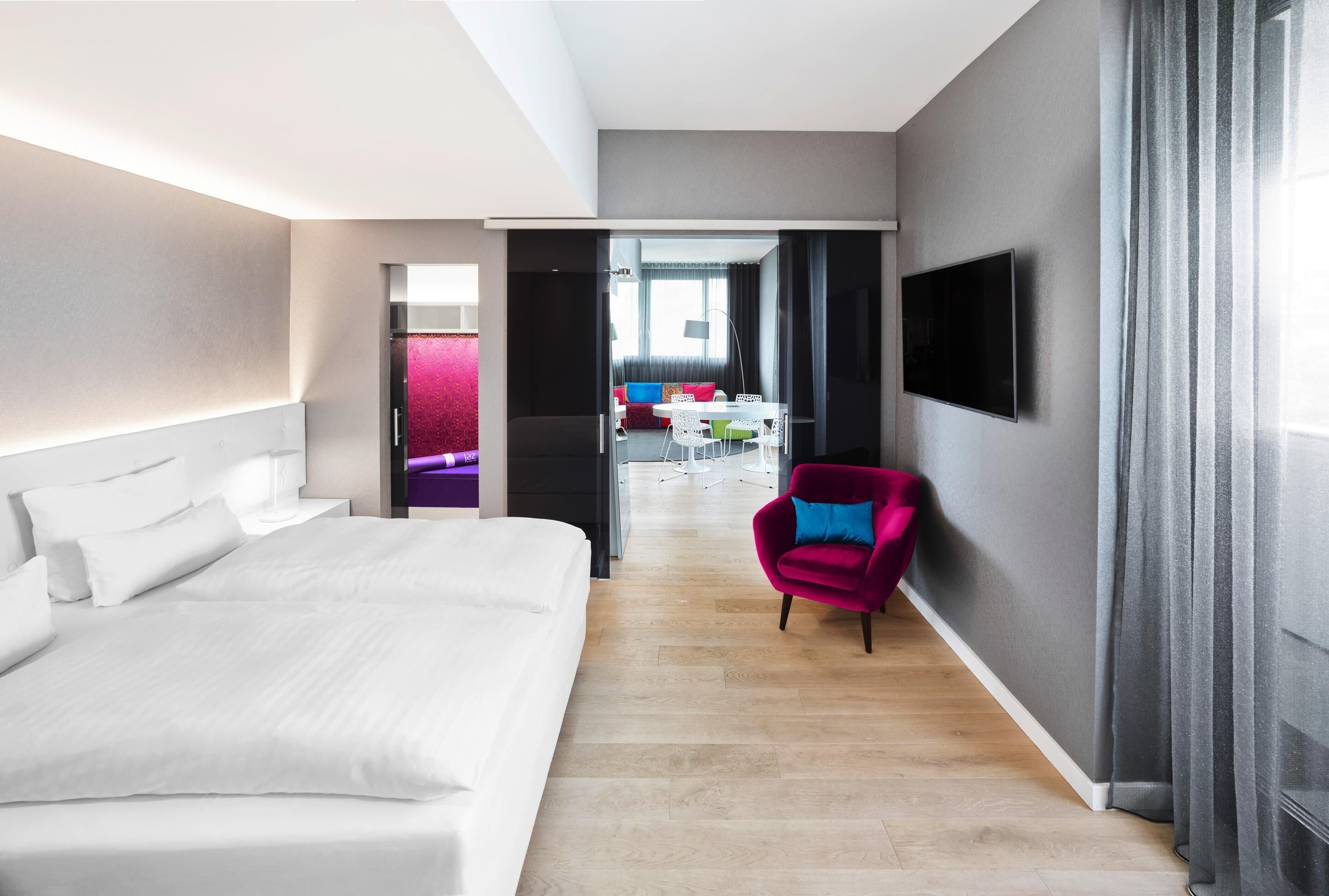 Ein modernes Hotelzimmer mit einem großen Bett, einem an der Wand befestigten Fernseher und Blick in den Speisesaal.