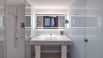 Un baño moderno con cabina de ducha de vidrio, tocador blanco con espejo y perchero.