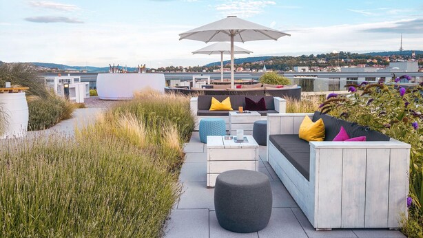 An outdoor seating area with a sofa, ottoman, and umbrella, overlooking a cityscape. - Jaz in the City Stuttgart (Stuttgart)