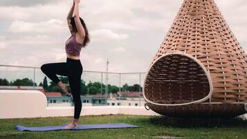 A person performing a yoga pose on a mat outdoors with a unique conical structure nearby.