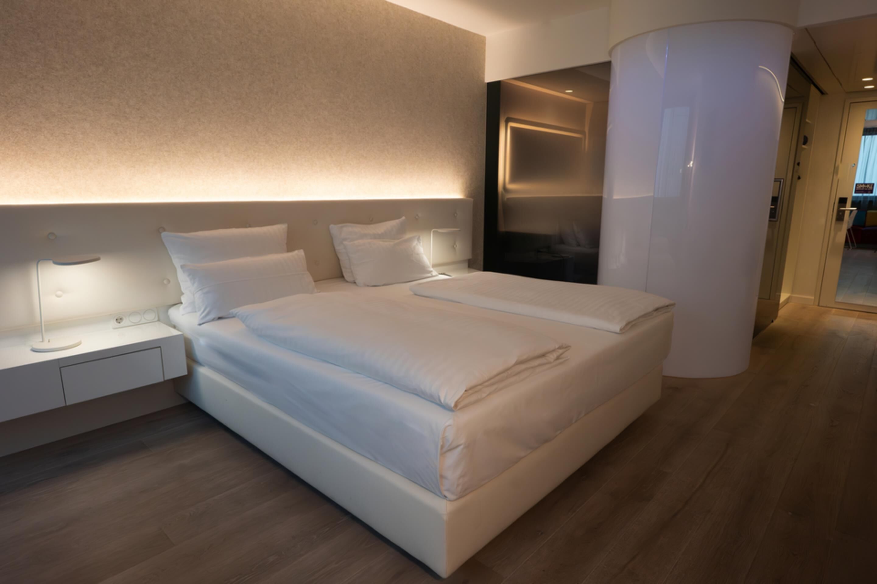 Une chambre d’hôtel moderne avec un grand lit, des tables de chevet, un téléviseur fixé au mur et une grande colonne.