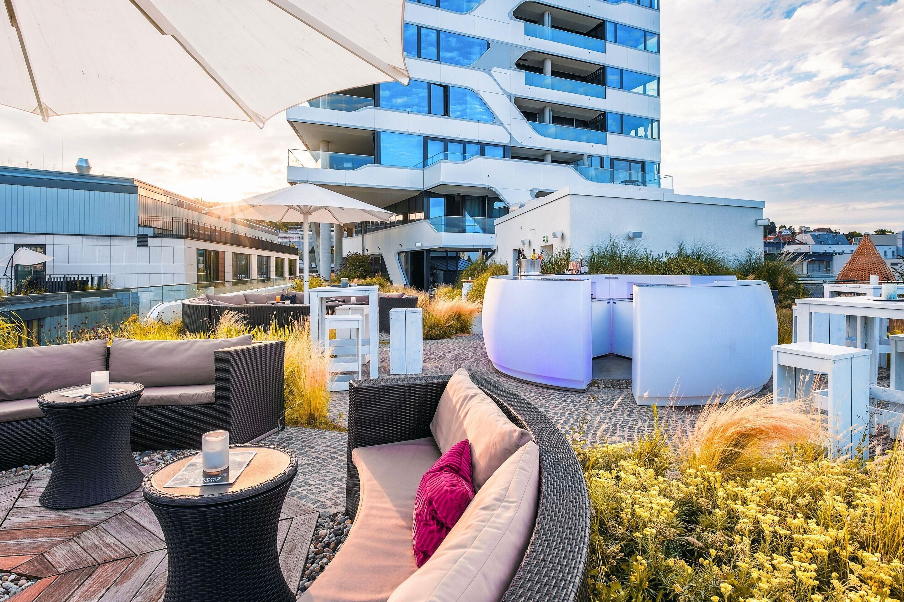A rooftop terrace with outdoor seating, a modern building in the background, and a clear sky.