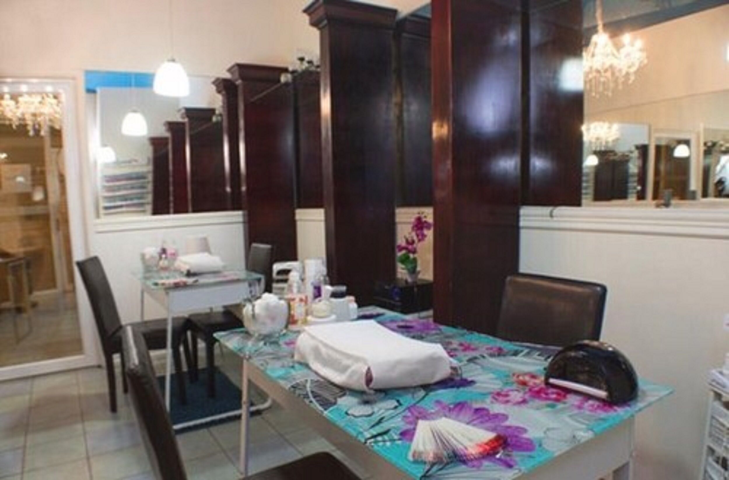 Un salon avec un miroir, des fauteuils, une table recouverte d’une nappe à motifs floraux et un lustre.