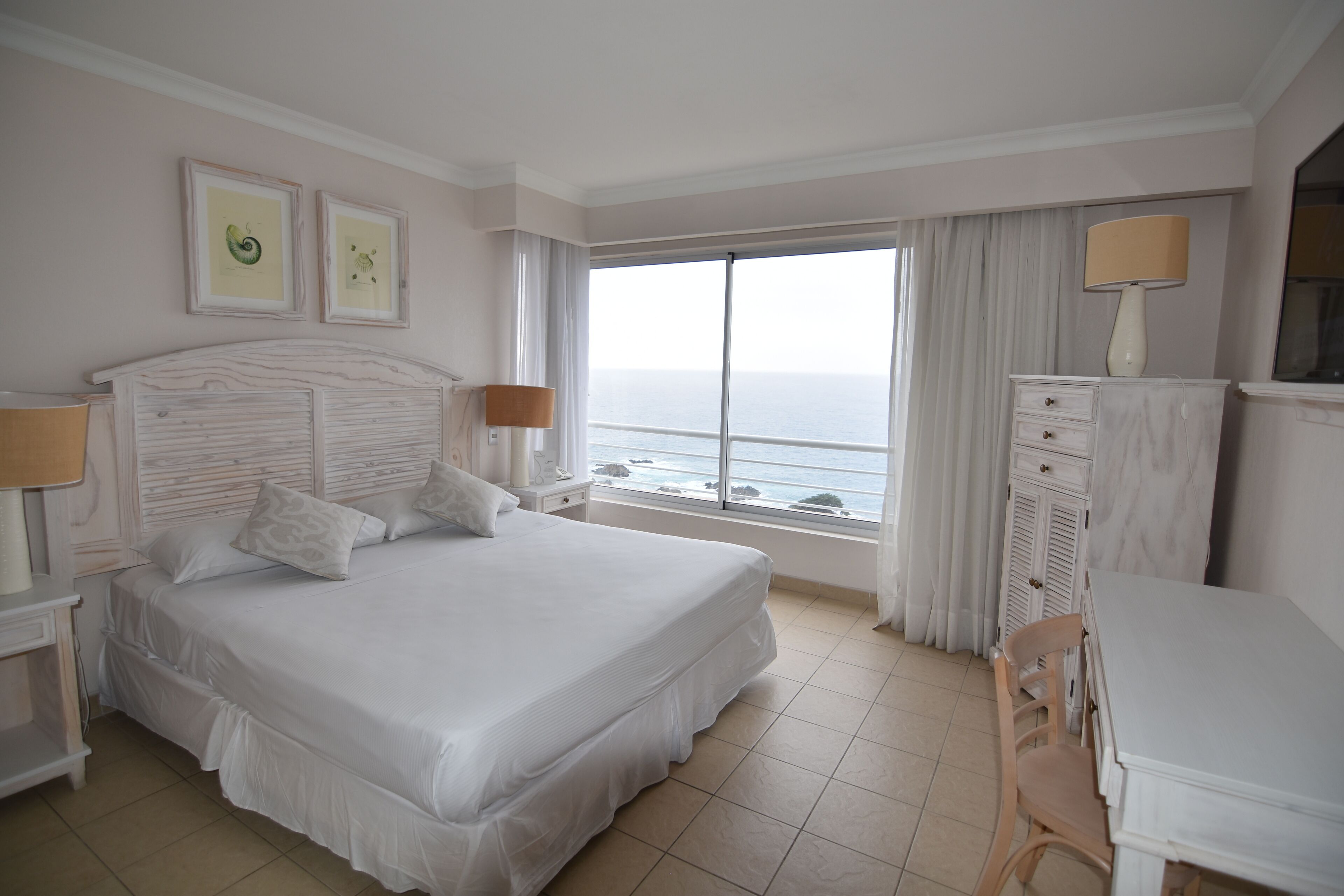 Una habitación de hotel con una cama grande, un escritorio y vista al mar.