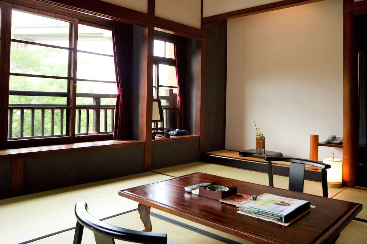 A traditional Japanese room with tatami flooring, a low table, a cushioned bench, and a hanging light fixture.