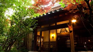 A traditional Japanese building with a wooden entrance, stone pathway, and surrounding greenery.