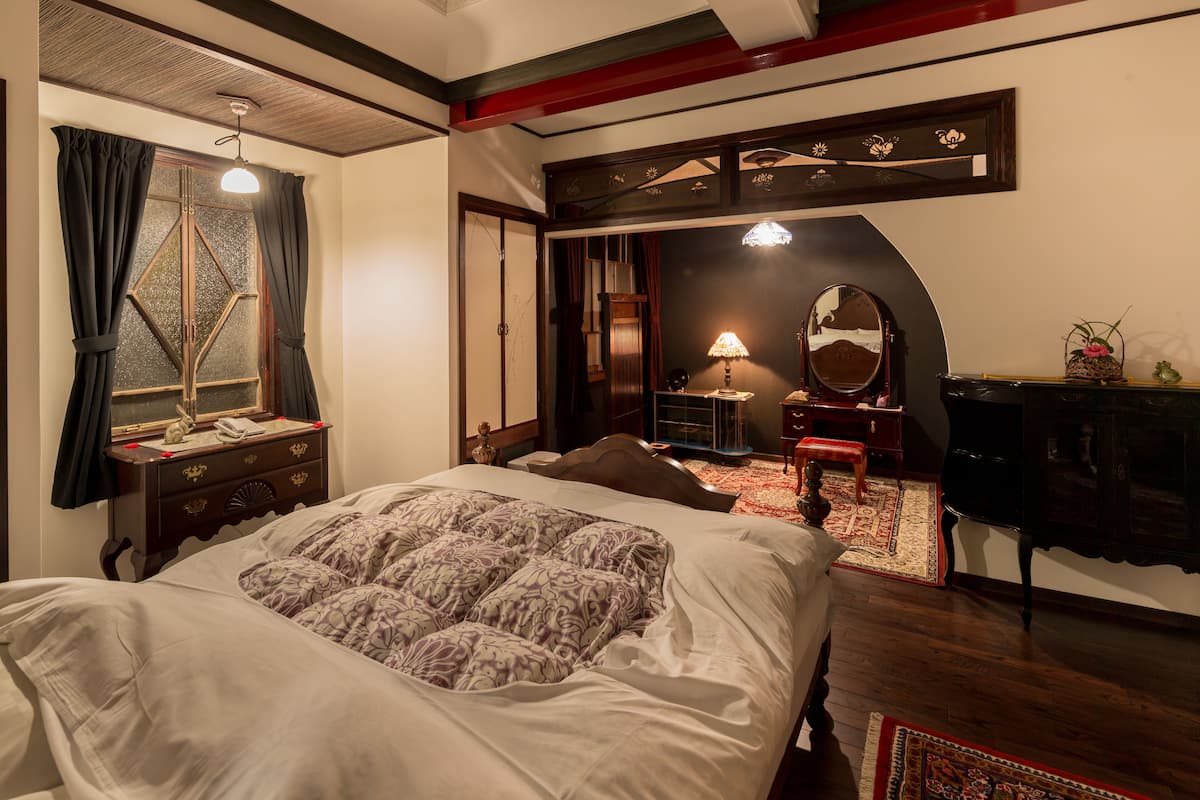 A bedroom with a large bed, a dresser, a desk, a mirror, and a red armchair.