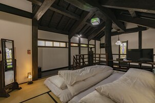 Una habitación tradicional japonesa con suelo de tatami, techo bajo con vigas a la vista, televisor y un pequeño santuario.