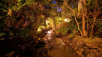 A stone pathway through a forested area with trees and a small stream.