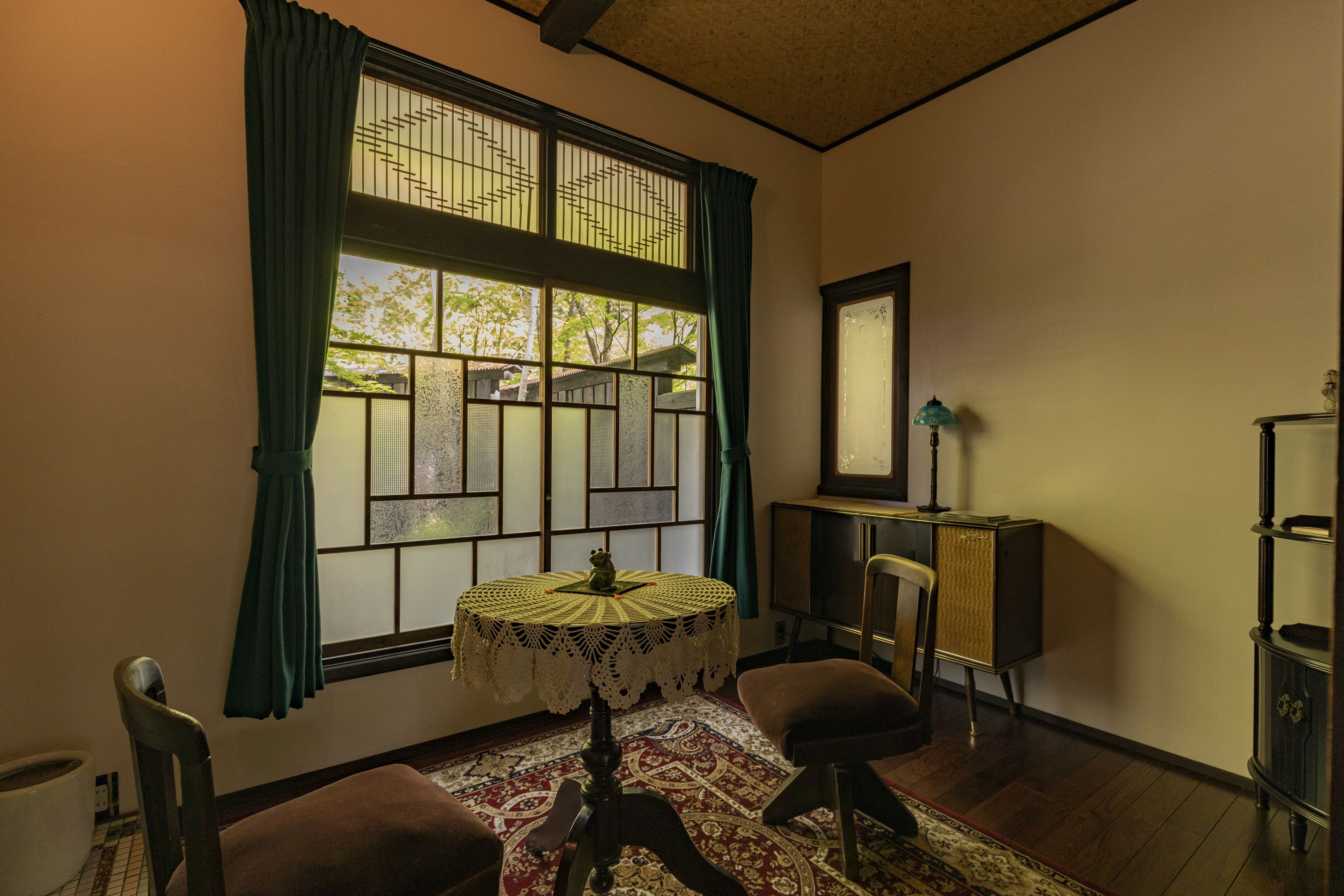 Una habitación con una mesa redonda, una silla, un armario y una ventana con cortinas.