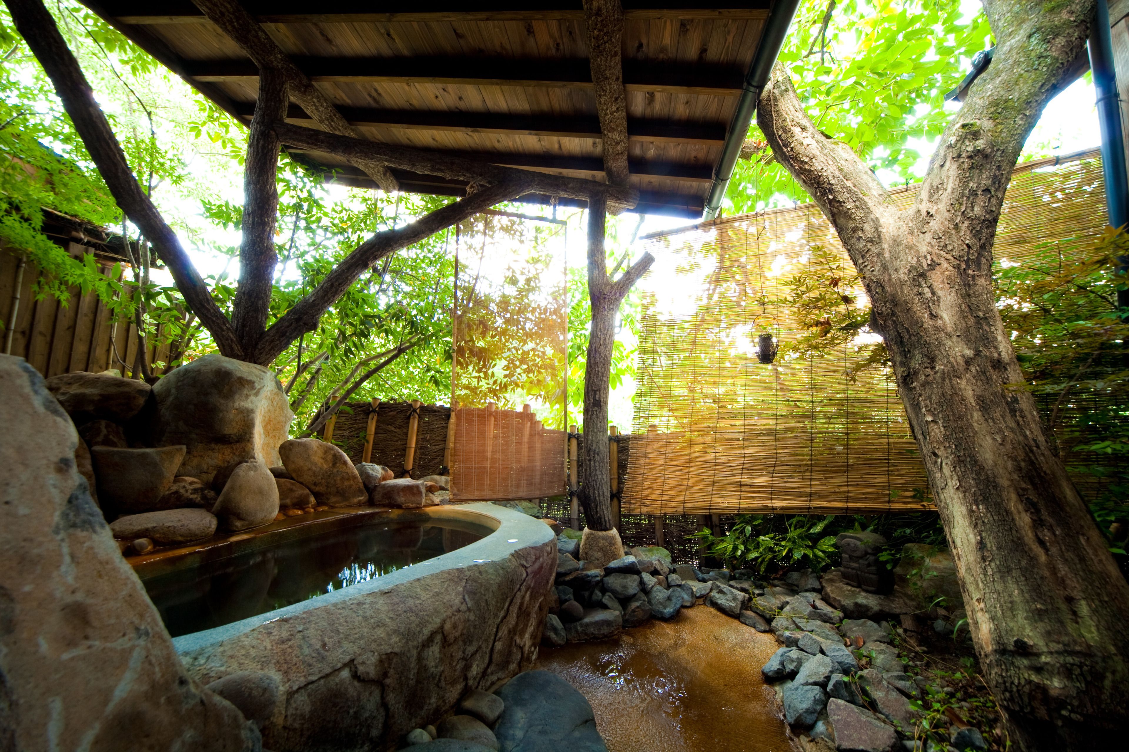 A traditional Japanese garden with a stone hot spring, bamboo fence, and a wooden pergola.