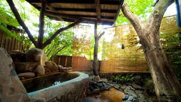 A traditional Japanese garden with a stone hot spring, bamboo fence, and a wooden pergola.
