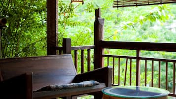A wooden deck with a bench and a round table, surrounded by lush greenery.