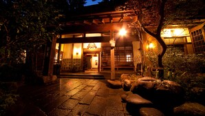 A traditional Japanese building with a wooden entrance, stone pathway, and illuminated interior.