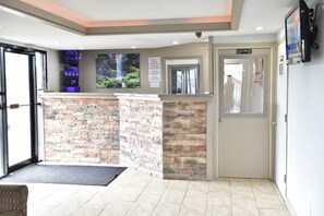 A reception area with a stone counter, a large window, and a door leading to the hallway. - Knights Inn Merrillville (Merrillville)