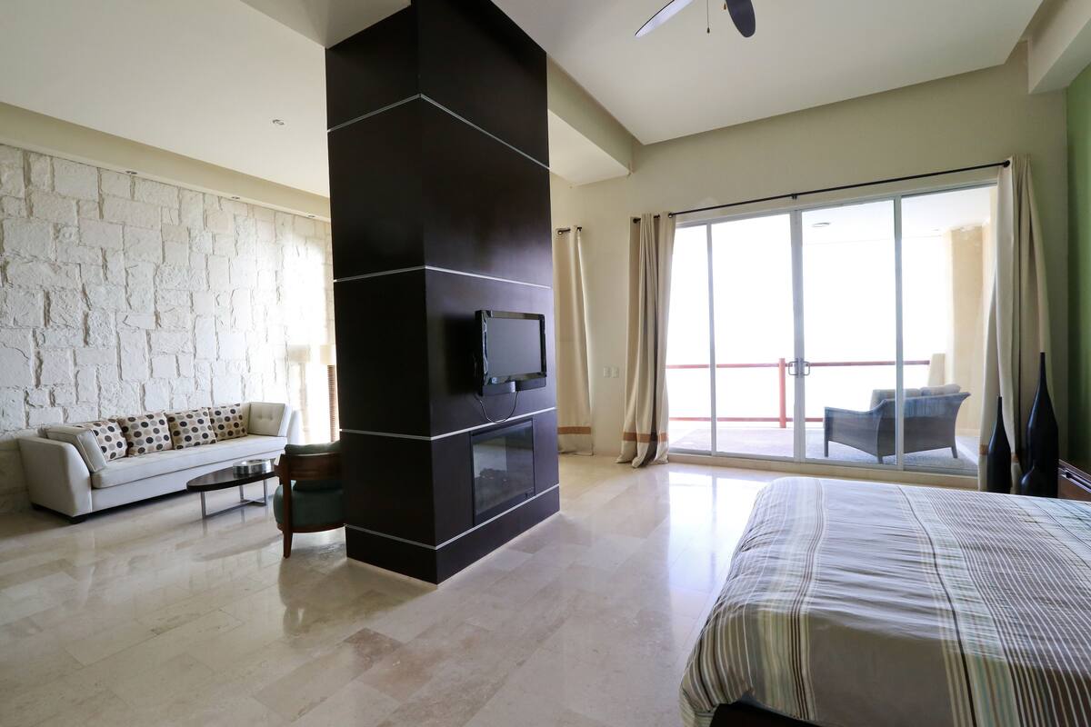 Una habitación de hotel moderna con una cama grande, un sofá, un televisor de pantalla plana, una chimenea y un balcón con vistas.