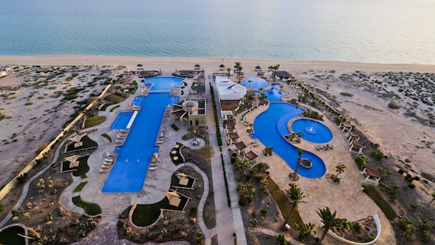 Luchtbeeld van een resort met diverse zwembaden, een strand en een woestijnlandschap.