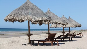 Een strand met rieten parasols en houten ligbedden.