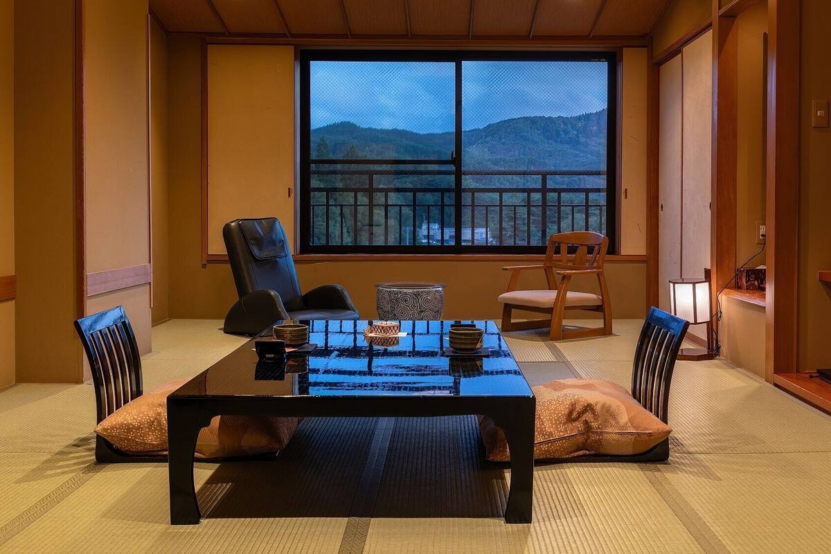 Une pièce de style japonais traditionnel, avec un sol recouvert de tatamis, une table basse et une grande fenêtre donnant sur les montagnes.