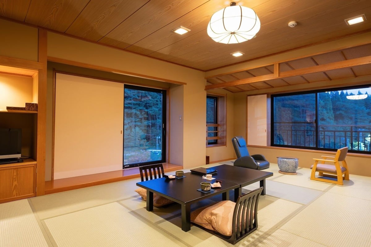 Une pièce de style japonais traditionnel, avec un sol recouvert de tatamis, une table basse, un téléviseur et de grandes fenêtres.