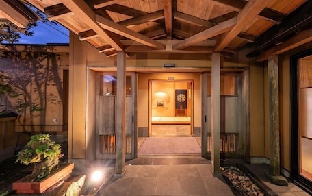 A traditional Japanese-style entrance with a wooden structure, a tiled pathway, and a lit interior.