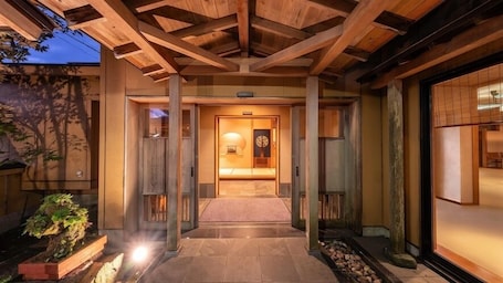 A traditional Japanese-style entrance with a wooden structure, a tiled pathway, and a lit interior.