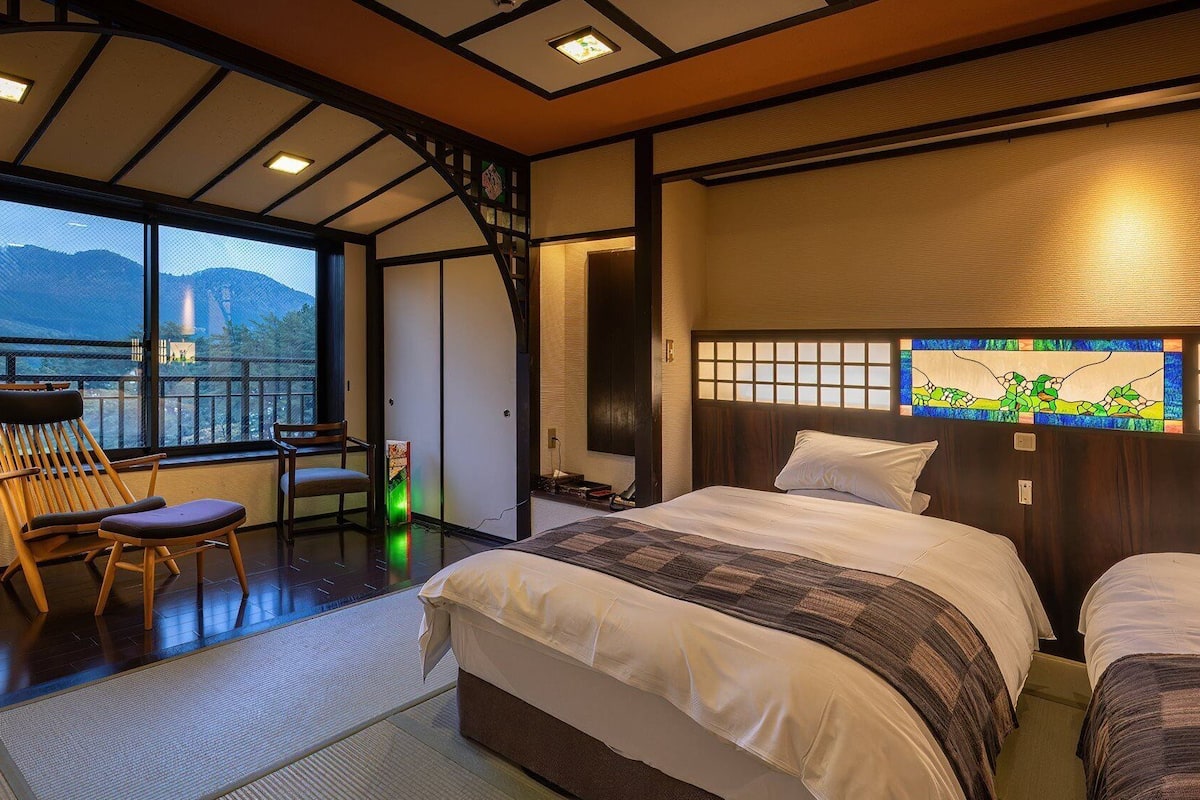 Une chambre d’hôtel avec une grande fenêtre, un lit, une chaise et une petite table.