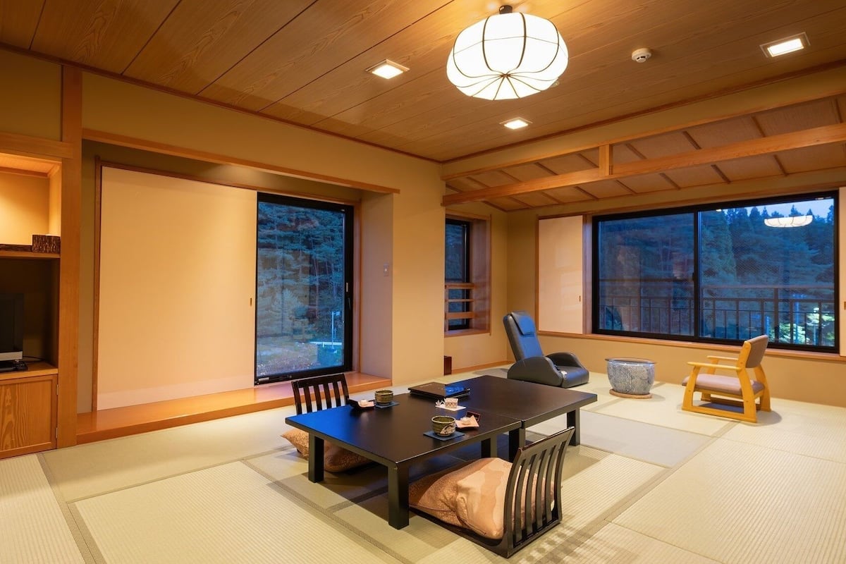 Une pièce de style japonais traditionnel, avec un sol recouvert de tatamis, une table basse, un téléviseur et de grandes fenêtres.