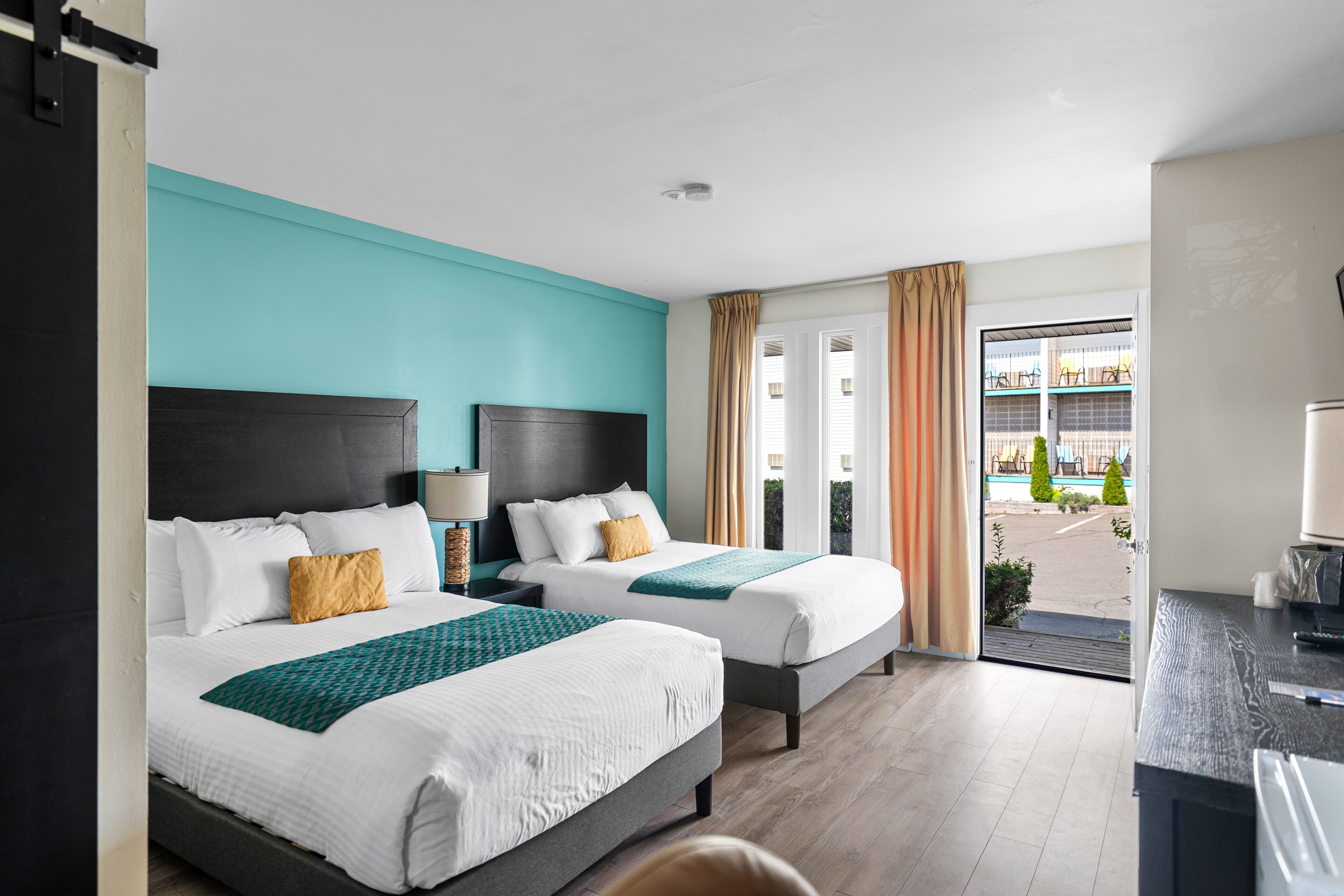 A hotel room with two beds, a desk, and a view of the outside.
