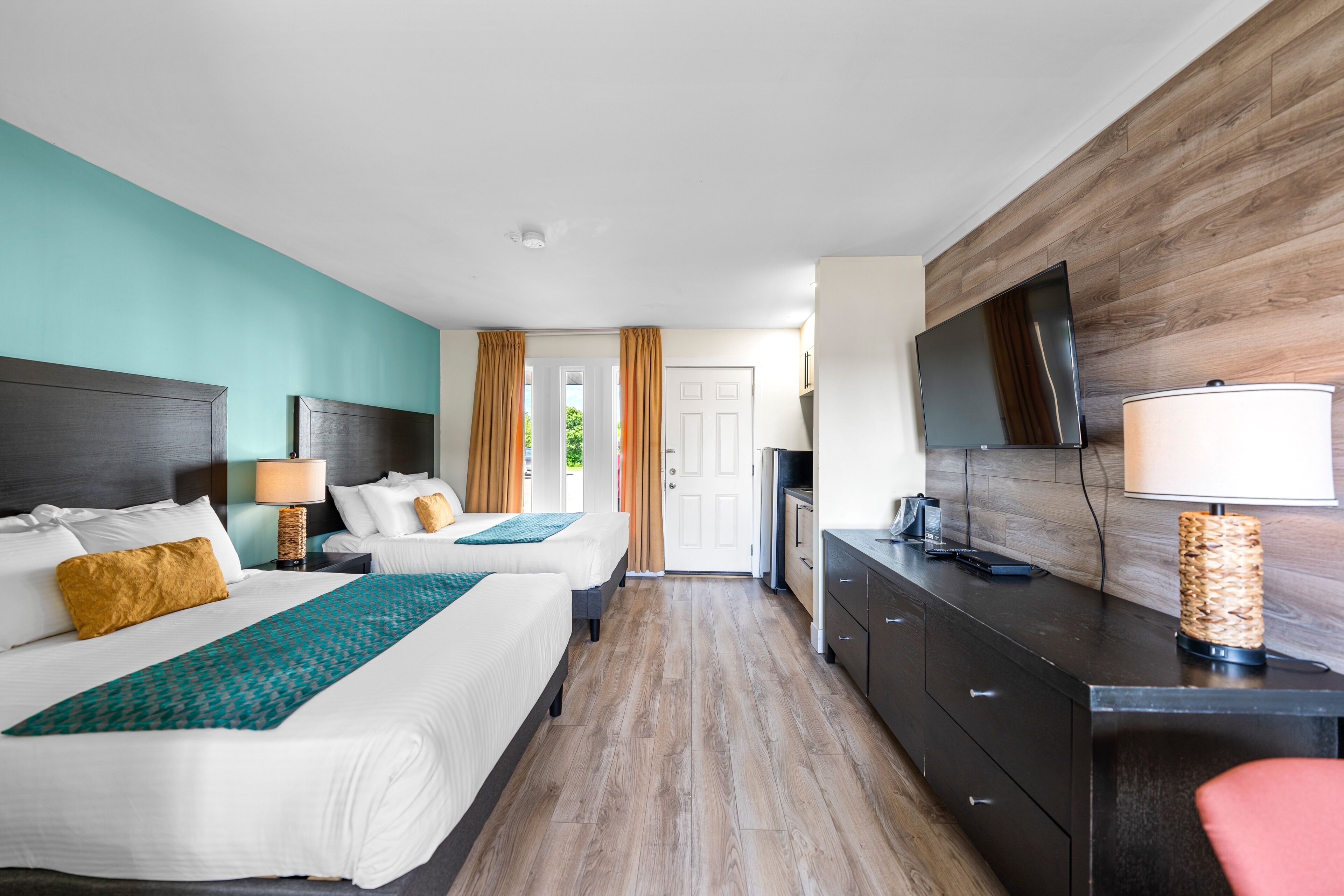 A hotel room with two beds, a desk, a TV, and a view of the outdoors.