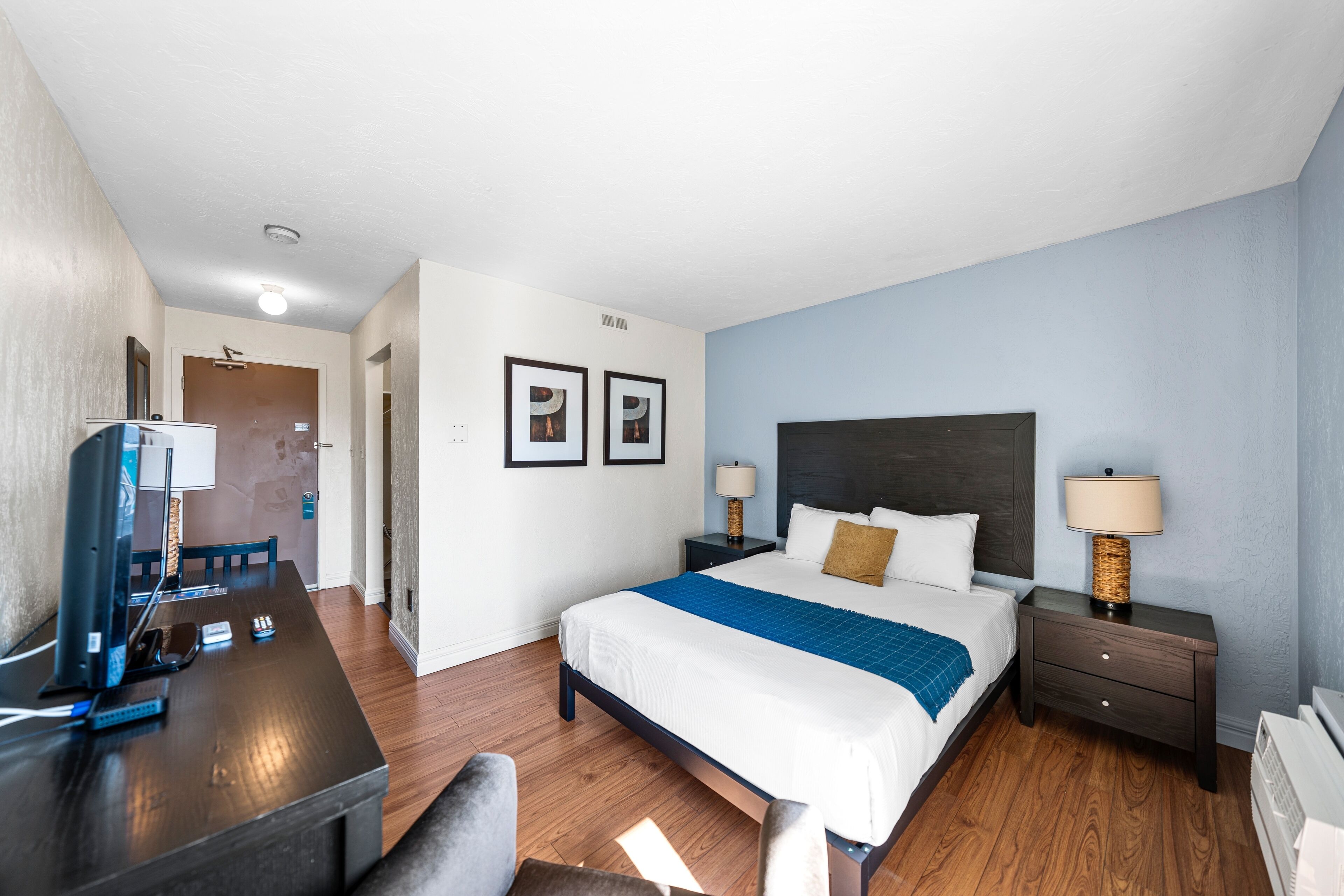 A hotel room with a bed, bedside tables, a desk with a computer, and a chair.
