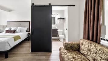 A hotel room with a bed, a sofa, a bathroom, and a sliding door.