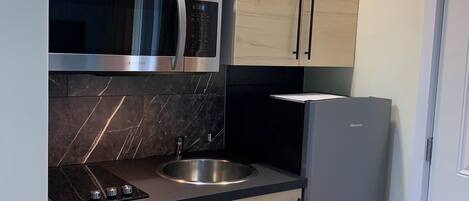 Une cuisine avec des meubles de couleur bois clair, un four à micro-ondes en acier inoxydable, un évier et un réfrigérateur.