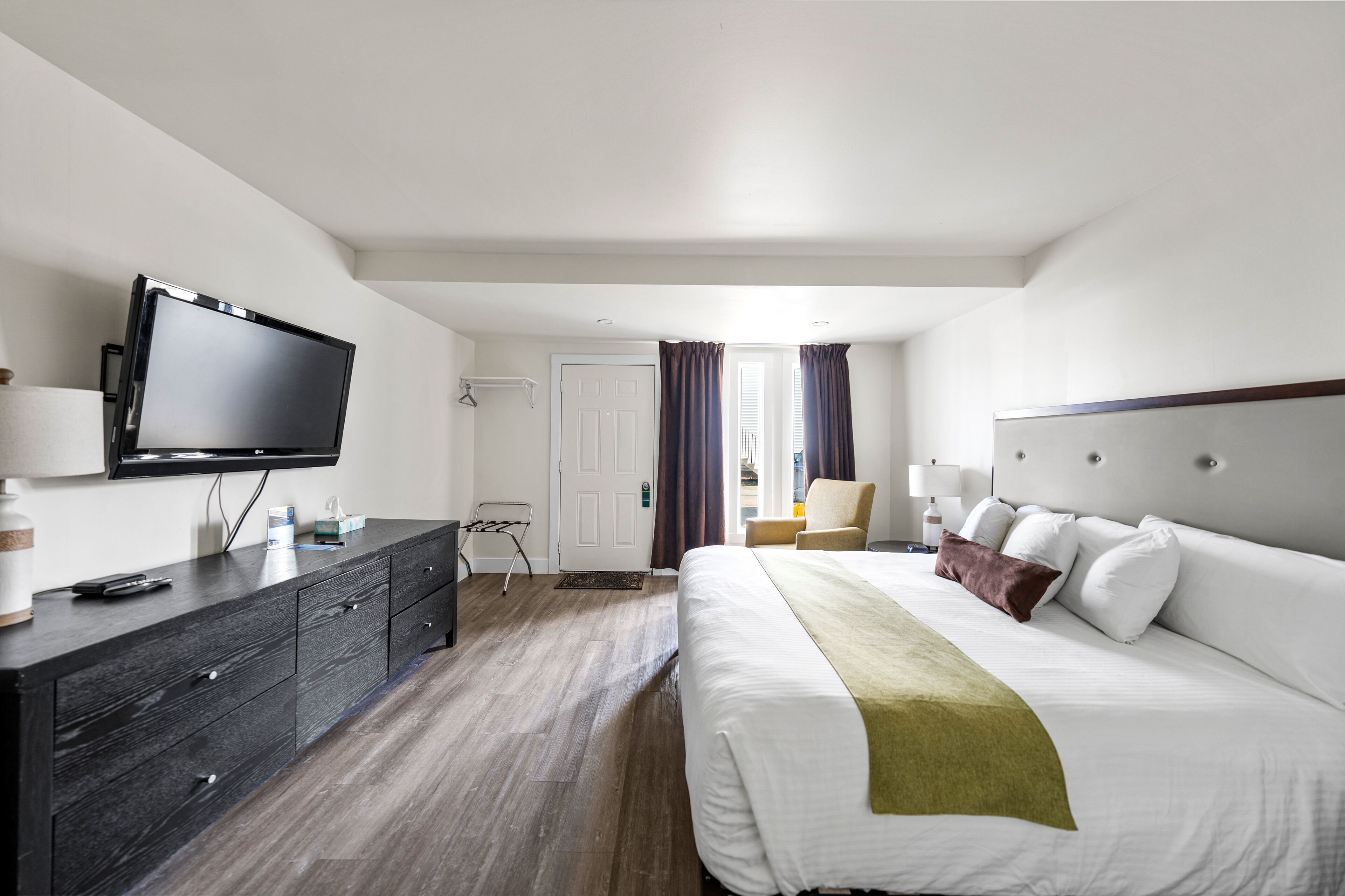 A hotel room with a large bed, a flat-screen TV mounted on the wall, a dark wooden dresser, and a chair.