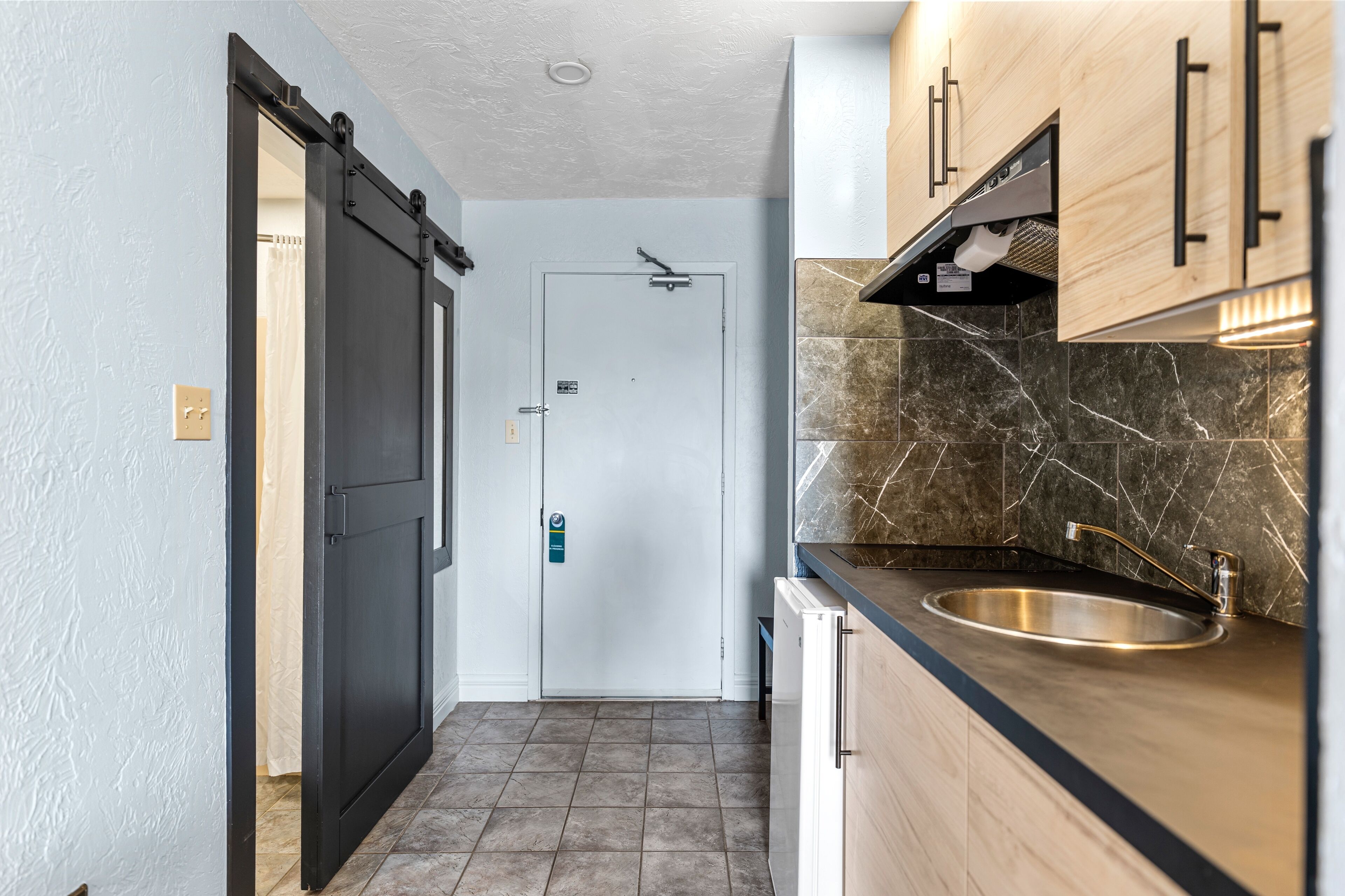 A modern kitchen with a sink, cabinets, and a door leading to another room.
