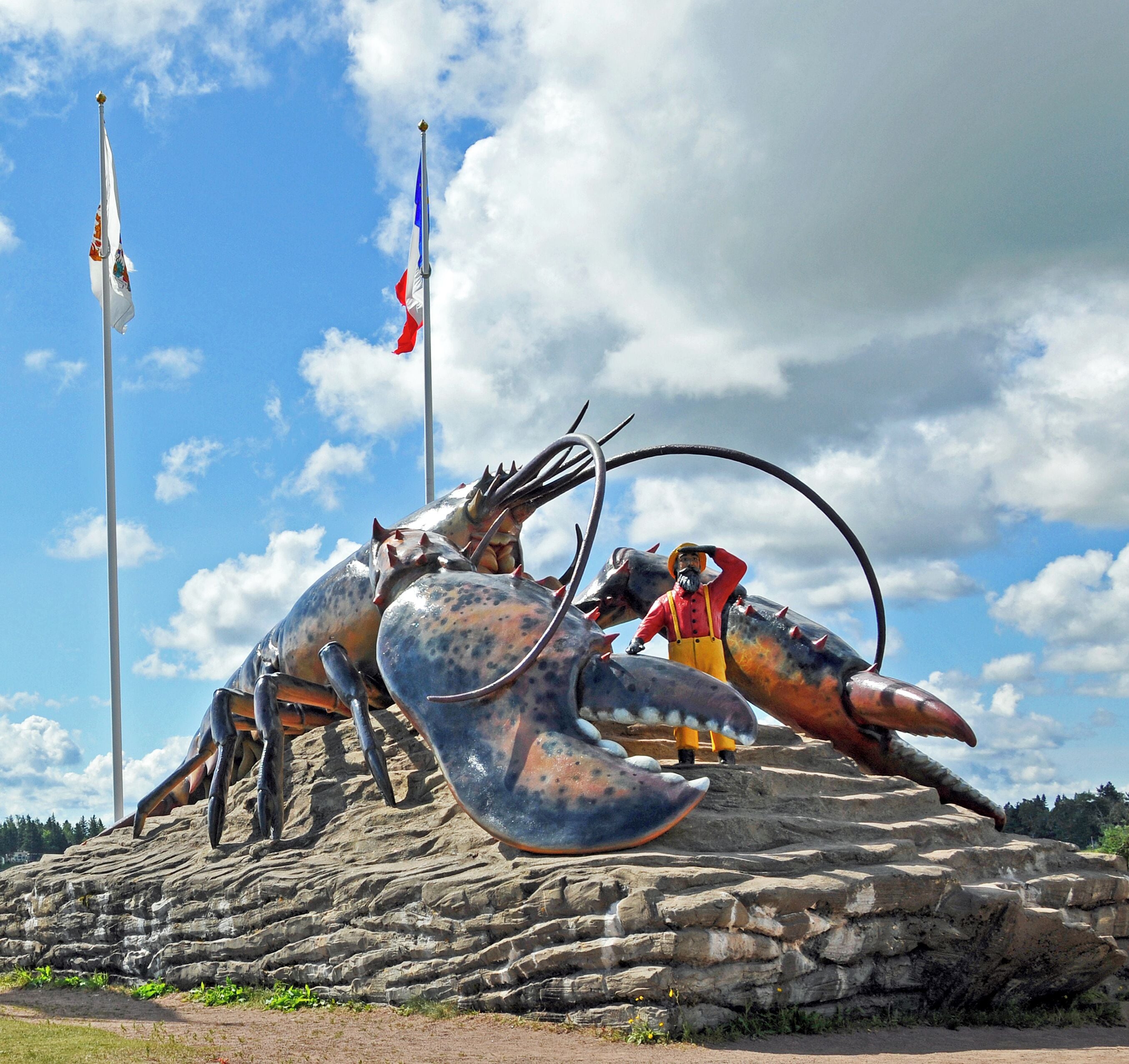 A large lobster sculpture on a rocky pedestal with a flagpole in the background.