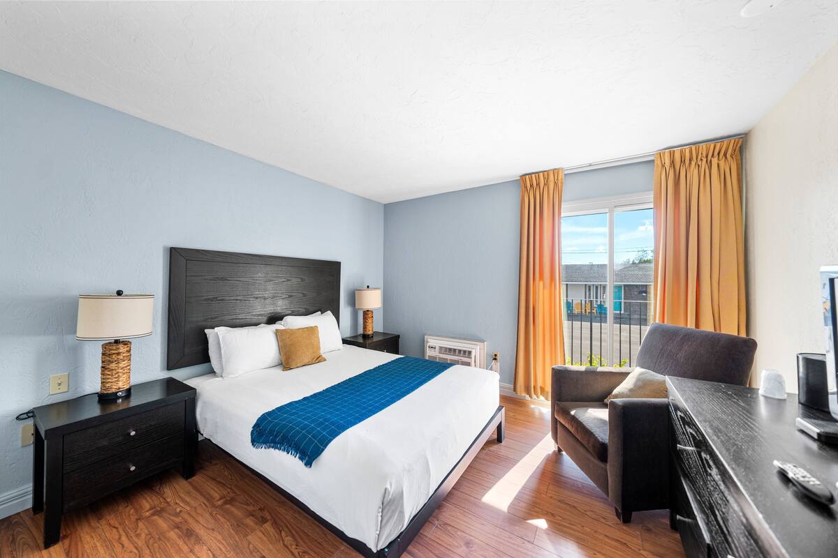 Ein Hotelzimmer mit einem großen Bett, einem Schreibtisch mit Stuhl, einem Fernseher und einem Fenster mit Vorhängen.