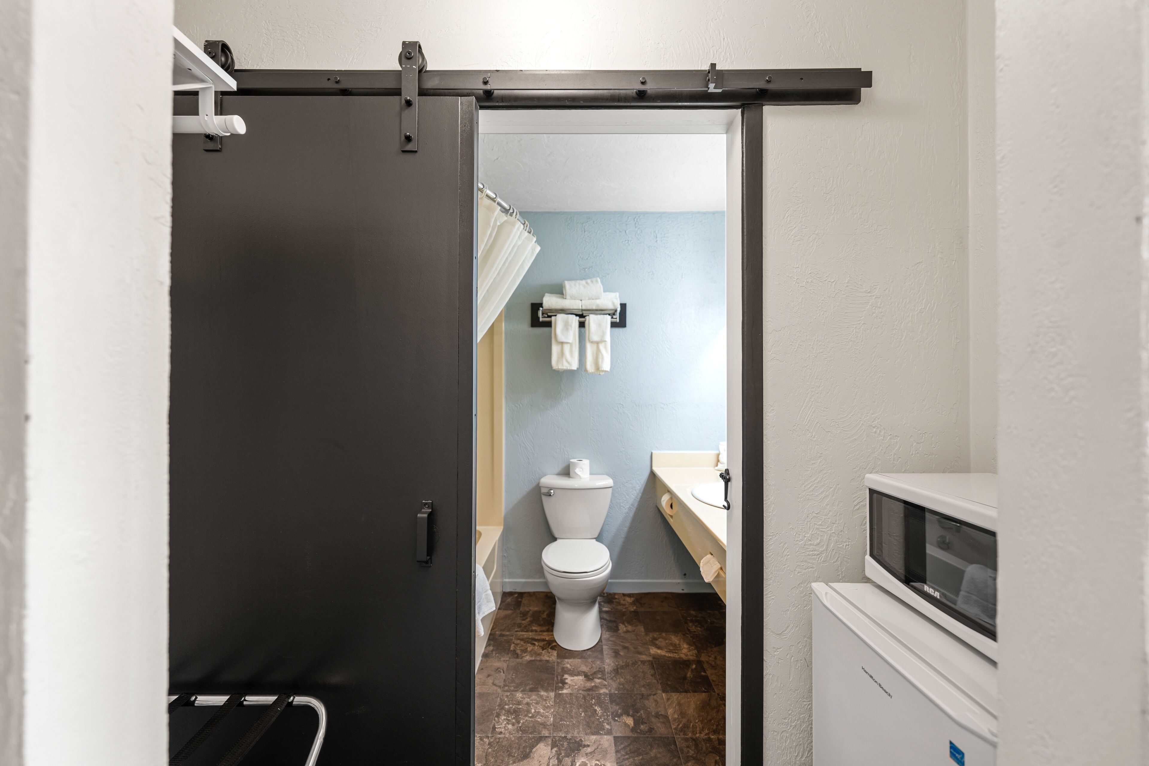 A bathroom with a toilet, a towel rack, and a microwave.
