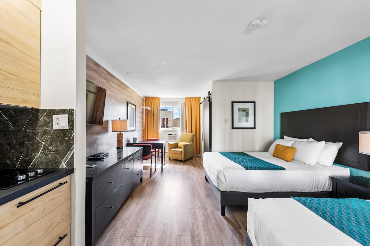 Ein Hotelzimmer mit Küchenzeile, einem Bett mit Kopfteil und einem Schreibtisch mit Stuhl.
