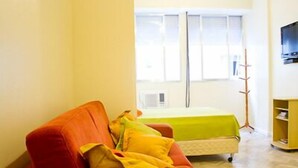 Ein Zimmer mit einer roten Couch, einem grünen Bett, einem gelben Nachttisch und einem an der Wand befestigten Fernseher.