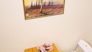 Ein kleiner Raum mit einem Holztisch, zwei weißen Stühlen und einem Baumgemälde an der Wand.