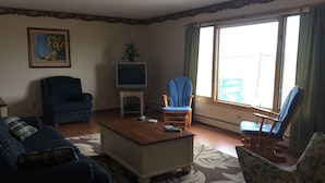 A living room with a sofa, a chair, a coffee table, a television, and a window with curtains. - Northwinds Motel (Northern Bruce Peninsula)