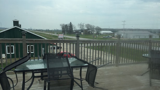 A wooden deck with a glass table and chairs, a green building in the background, and a fence separating the deck from the property. - Northwinds Motel (Northern Bruce Peninsula)