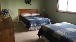 A bedroom with two beds, a wooden dresser, a nightstand, a lamp, and a window. - Northwinds Motel (Northern Bruce Peninsula)