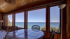 En inredning med träpanel, ett runt bord och stolar, stora fönster med utsikt över havet och en takfläkt.