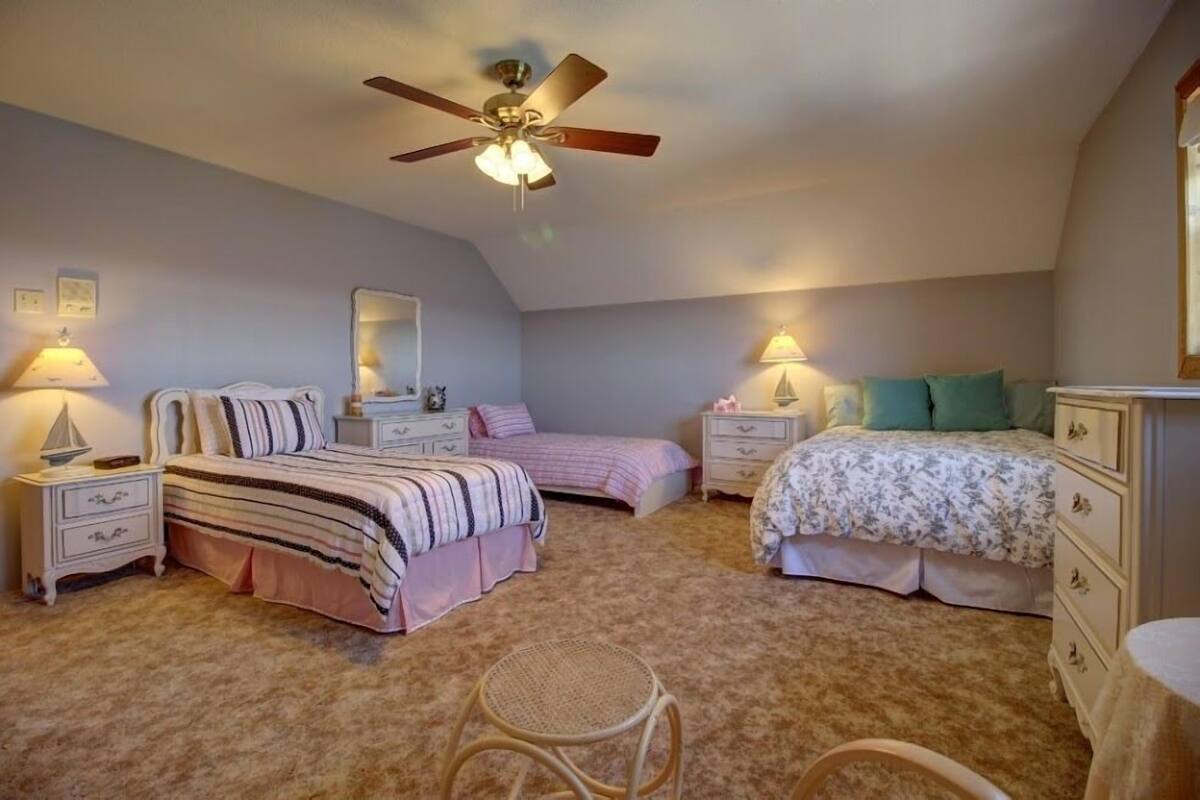 A bedroom with two beds, a ceiling fan, bedside lamps, a mirror, and a rattan chair.