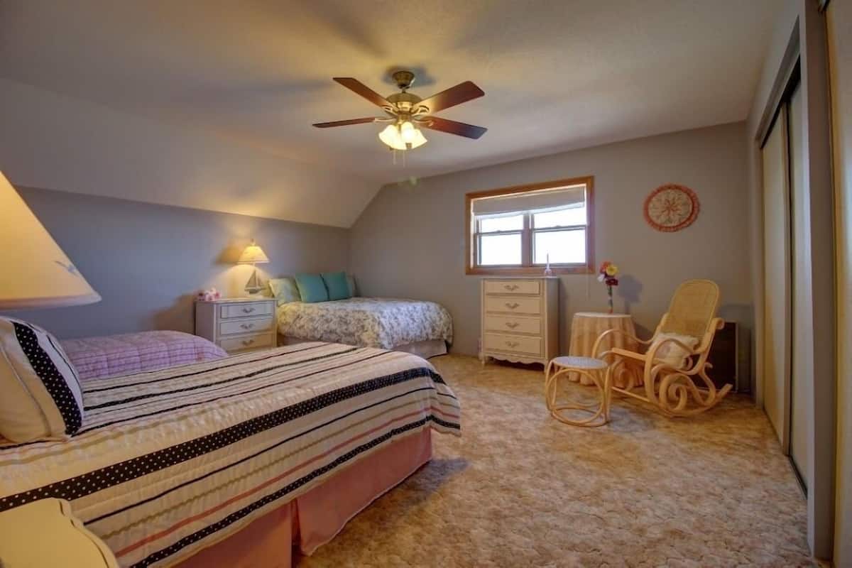 A bedroom with a bed, a chair, a dresser, a window, and a ceiling fan.