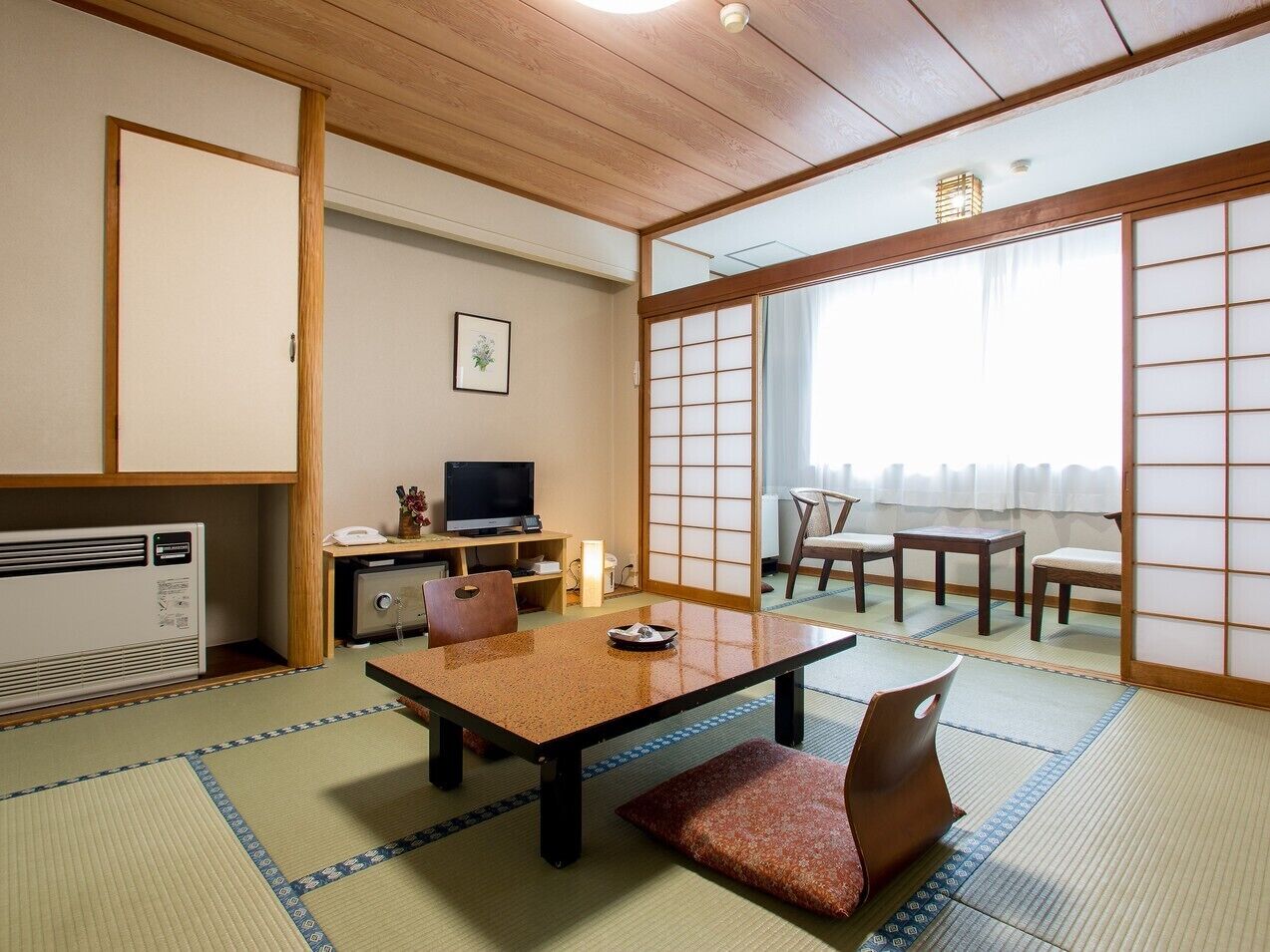 Um quarto japonês tradicional com tatames, uma mesa baixa, cadeiras, uma televisão e portas deslizantes.