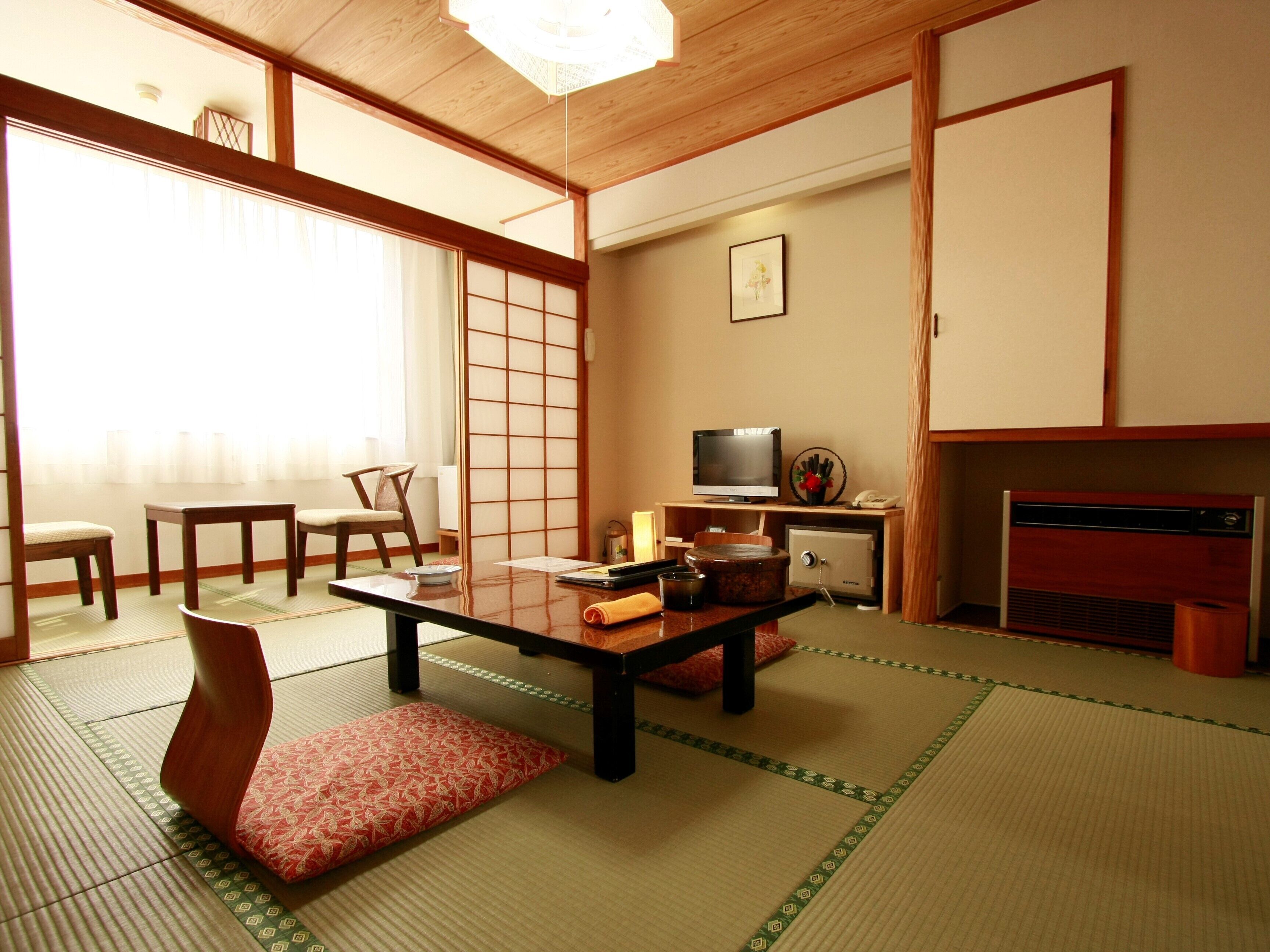 A traditional Japanese room with tatami flooring, a low table, chairs, a television, and a fireplace.